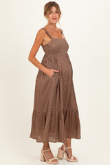 woman wearing a brown polka dot maternity dress with adjustable straps, a tiered skirt, and side pockets, showing her baby bump