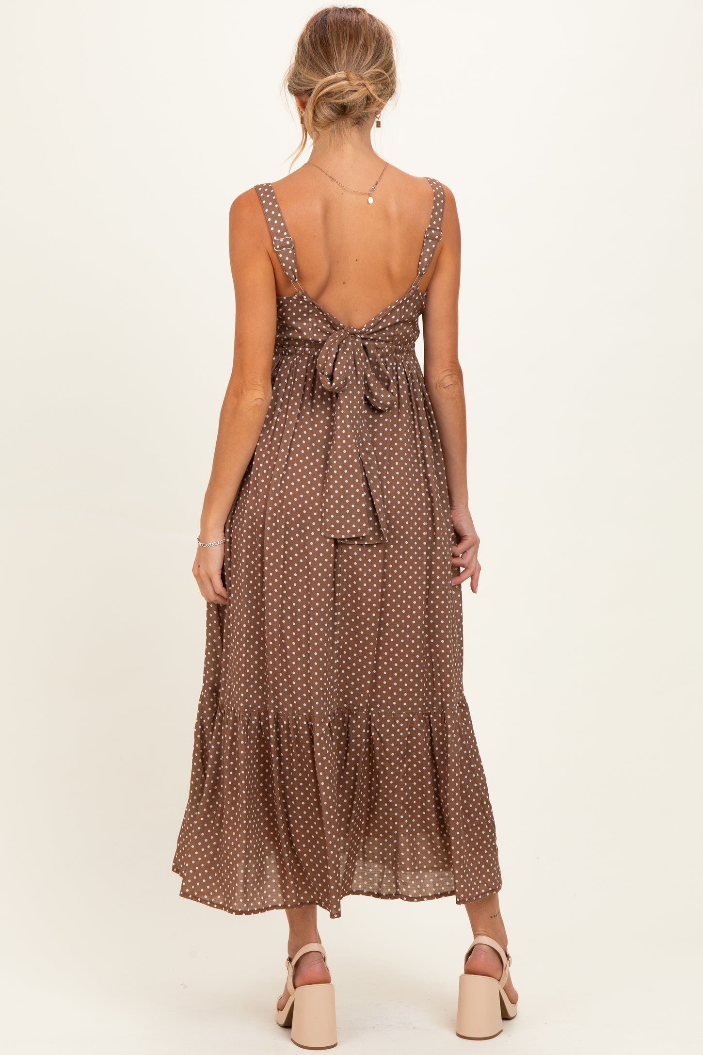 woman wearing a brown polka dot maternity dress with adjustable straps and a bow detail at the back