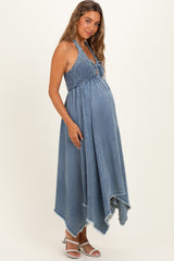 woman wearing a denim blue maternity maxi dress with a smocked bodice and a high-low hem, showcasing her baby bump