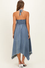 woman wearing a denim halter maternity dress with a smocked back and an asymmetrical hemline