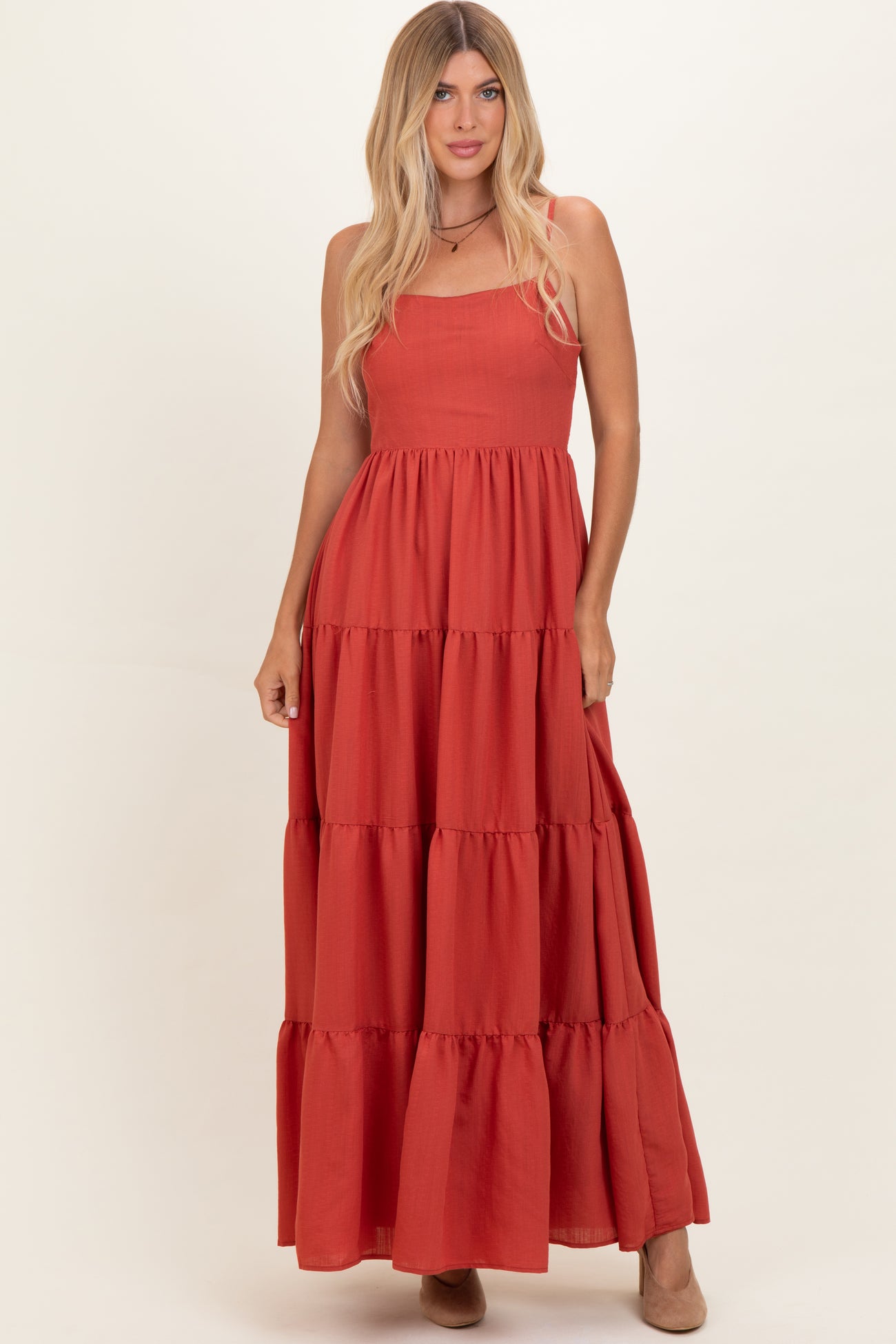 woman wearing a rust-colored maxi dress with tiered ruffles and spaghetti straps.