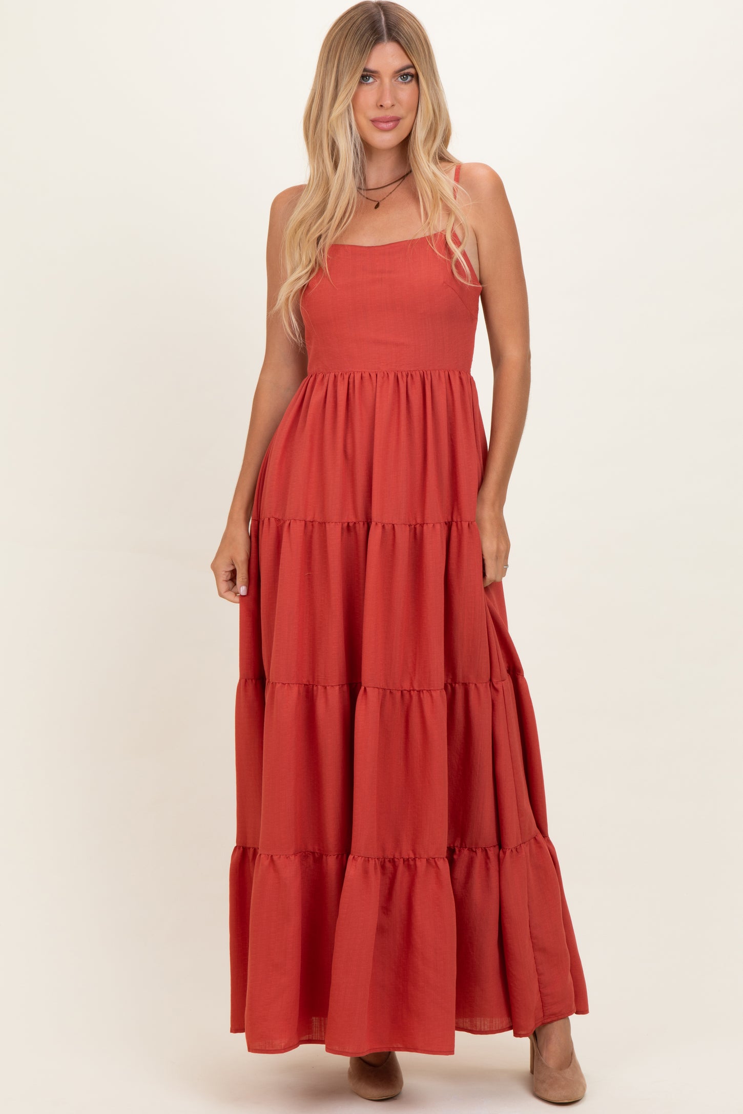 woman wearing a rust-colored maxi dress with tiered ruffles and spaghetti straps.