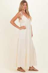 woman wearing a cream colored maxi dress with tie straps and tiered skirt, standing in profile with a relaxed pose