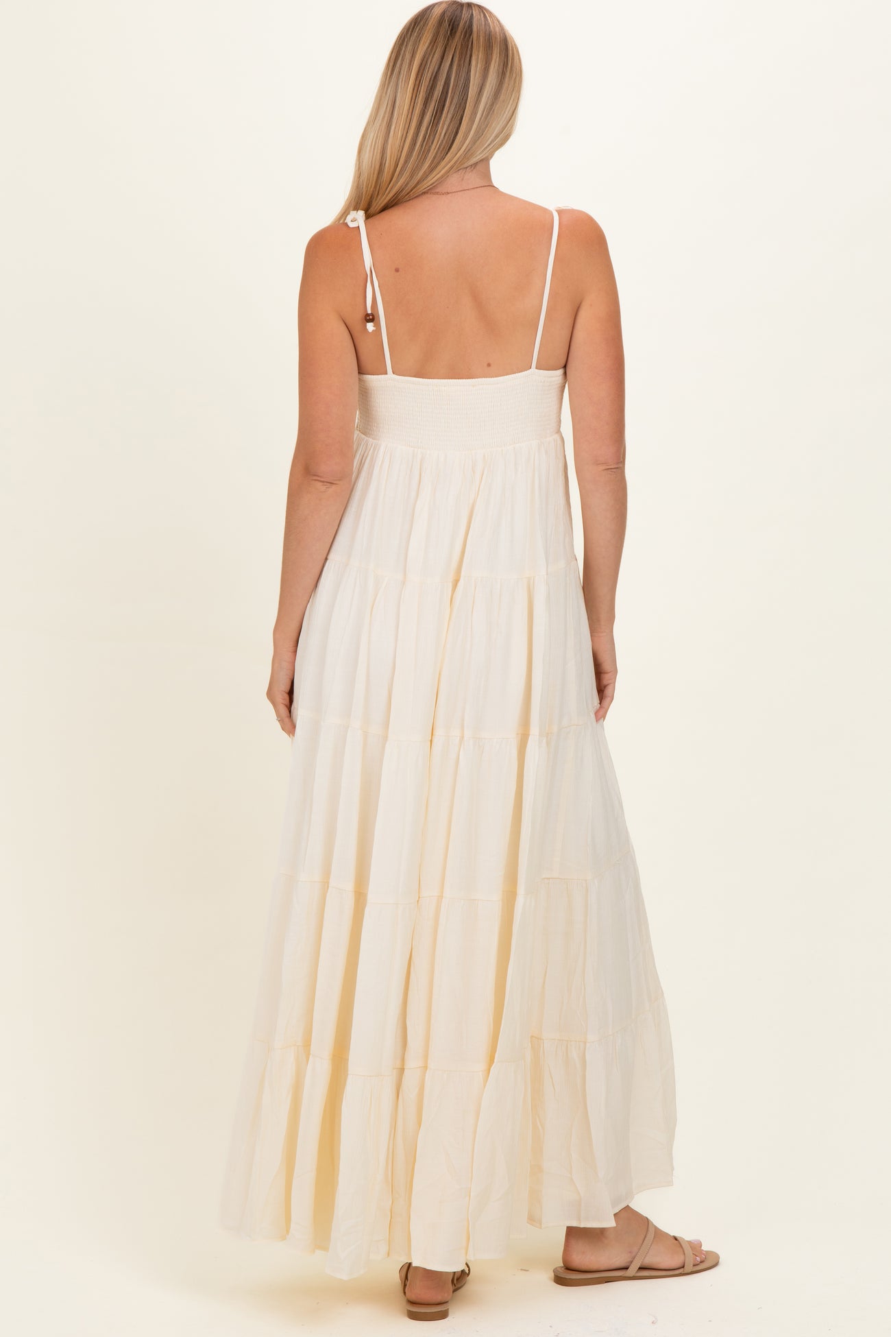 woman wearing a cream tiered maxi dress with adjustable straps and a smocked bodice, viewed from the back