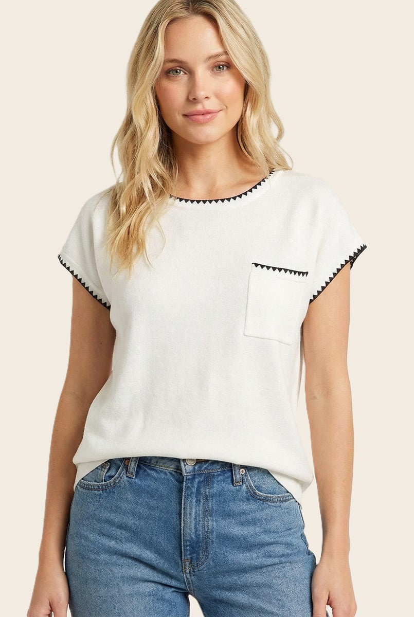 woman wearing a white short sleeve top with black trim and a chest pocket, paired with blue jeans