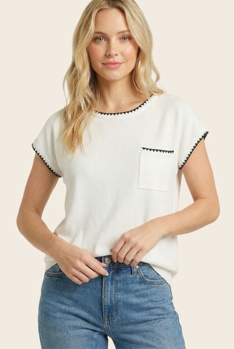 woman wearing a white short sleeve top with black trim and a front pocket, paired with blue jeans