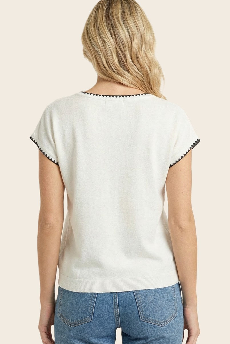 woman wearing a cream short sleeve sweater with black trim and blue high-waisted jeans