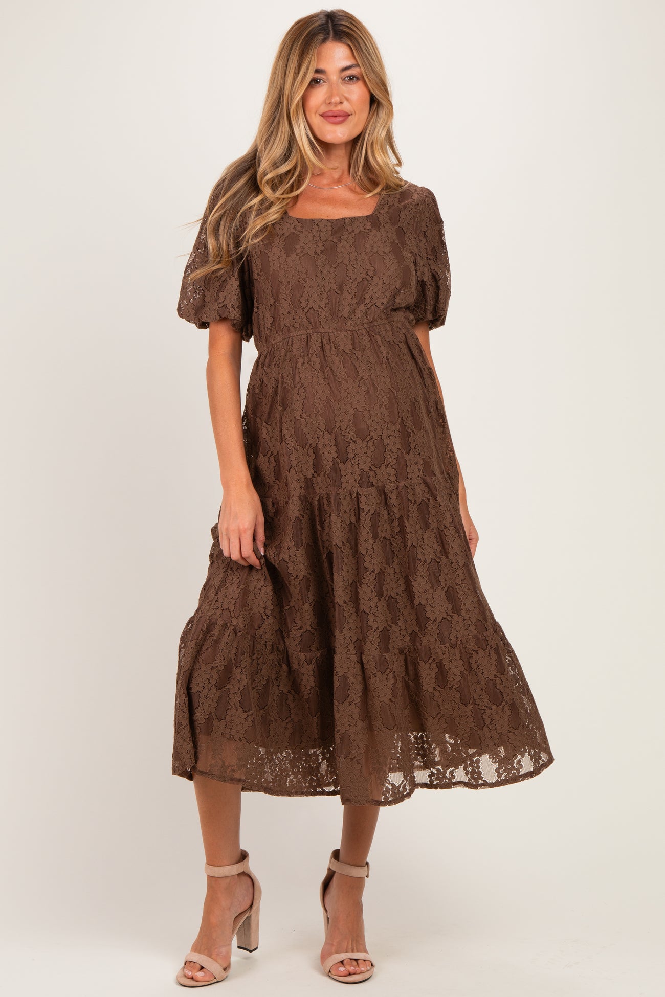 woman wearing a brown lace maternity dress with short puff sleeves and a flowing skirt, highlighting her baby bump