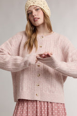 woman wearing a light pink oversized cardigan with buttons and a ribbed texture, styled with a pink polka dot skirt and a beige knit beanie