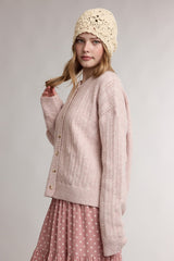 woman wearing a light pink knitted cardigan with buttons and a cream crochet beanie, styled with a polka dot pink skirt