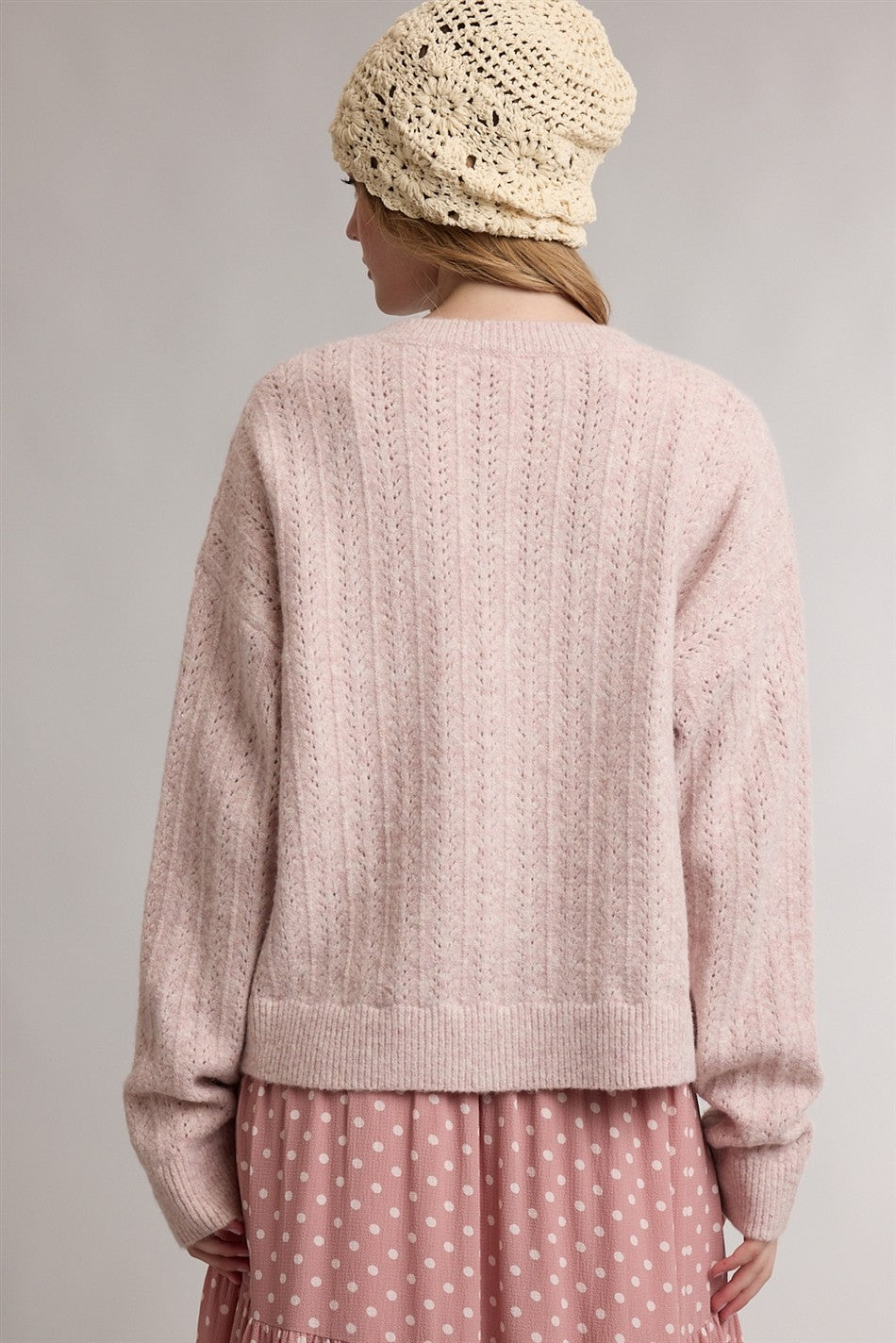woman wearing a light pink knitted sweater with a relaxed fit and a textured pattern, styled with a cream beanie