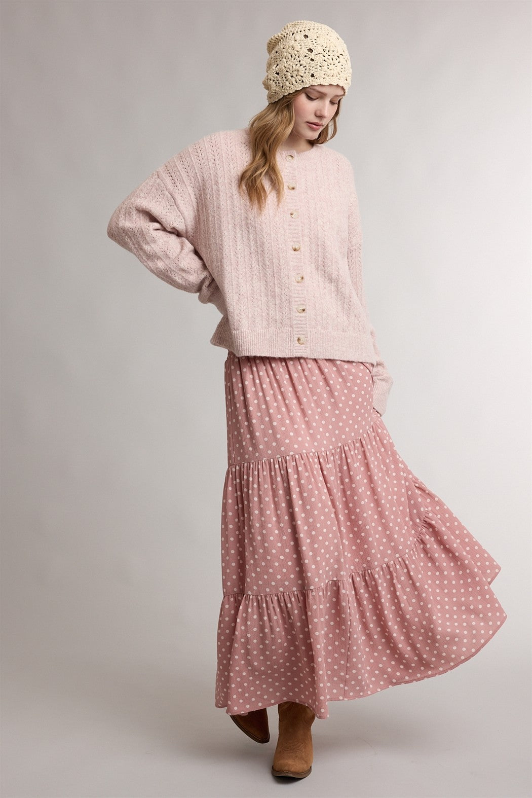 woman wearing a light pink knitted cardigan and a pink polka dot tiered maxi skirt with tan ankle boots