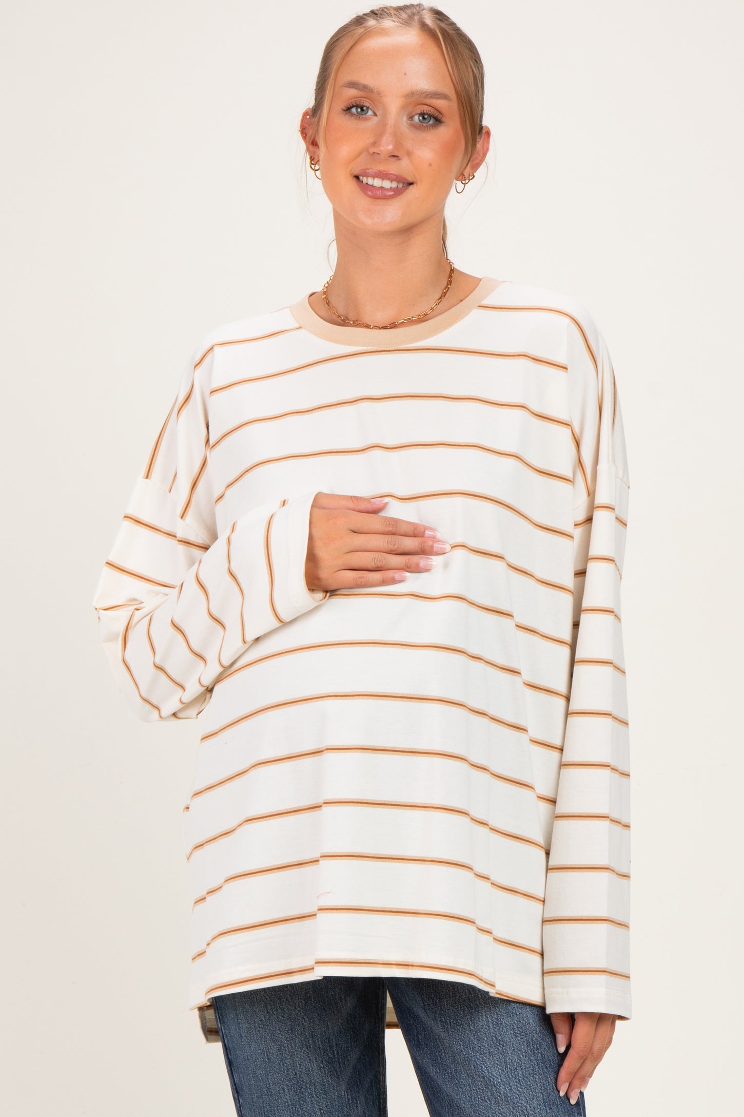 woman wearing a cream and brown striped maternity top and holding her baby bump