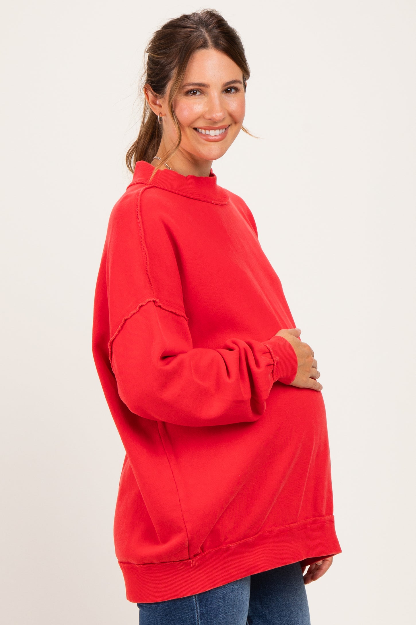 woman wearing a bright red oversized maternity sweatshirt and gently holding her baby bump