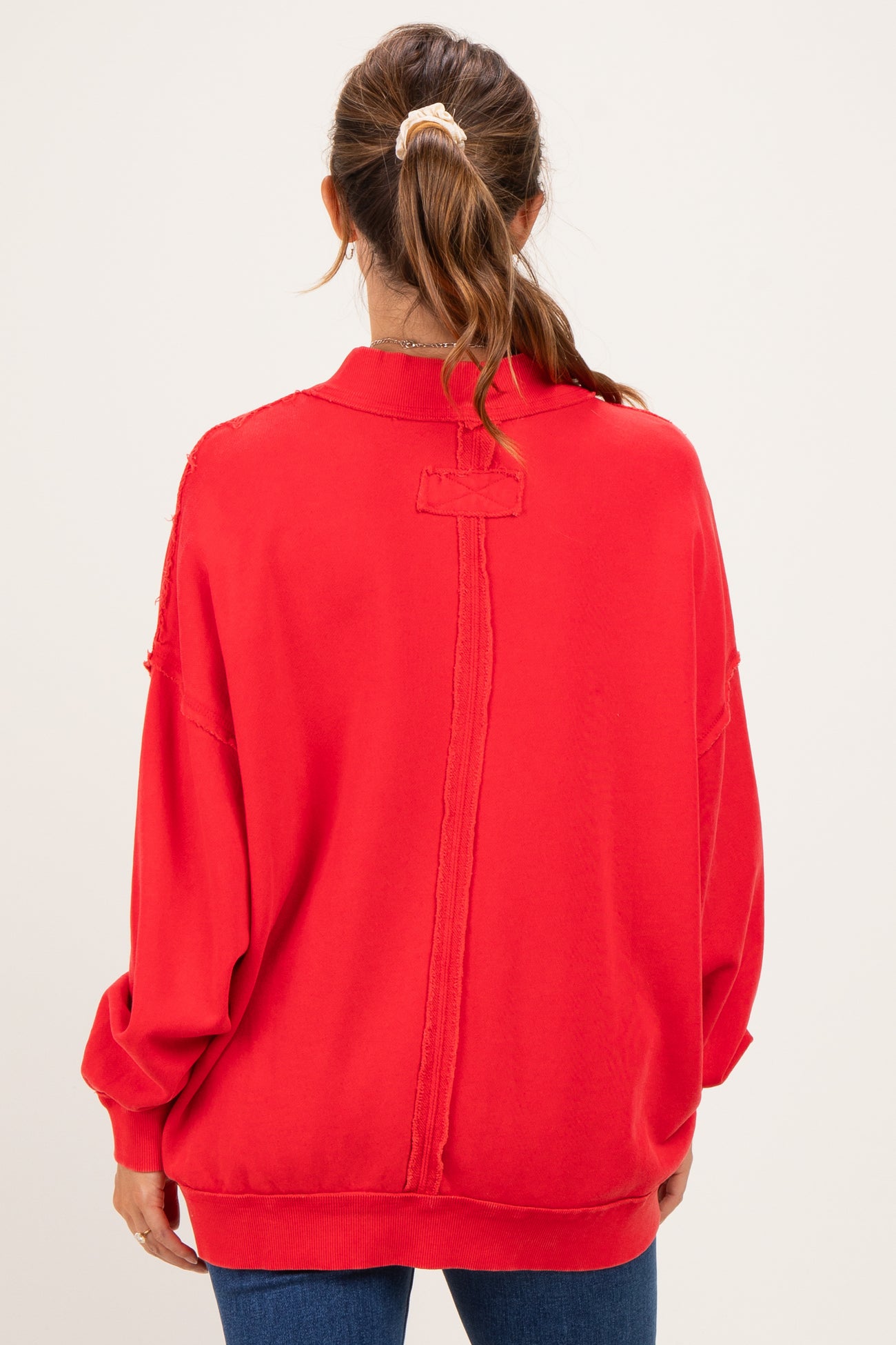 woman wearing a red oversized maternity sweatshirt with distressed details, viewed from the back