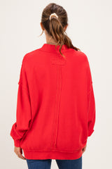 woman wearing a red oversized maternity sweatshirt with distressed details, viewed from the back