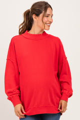 woman wearing a red oversized maternity sweatshirt with a high neckline and visible baby bump