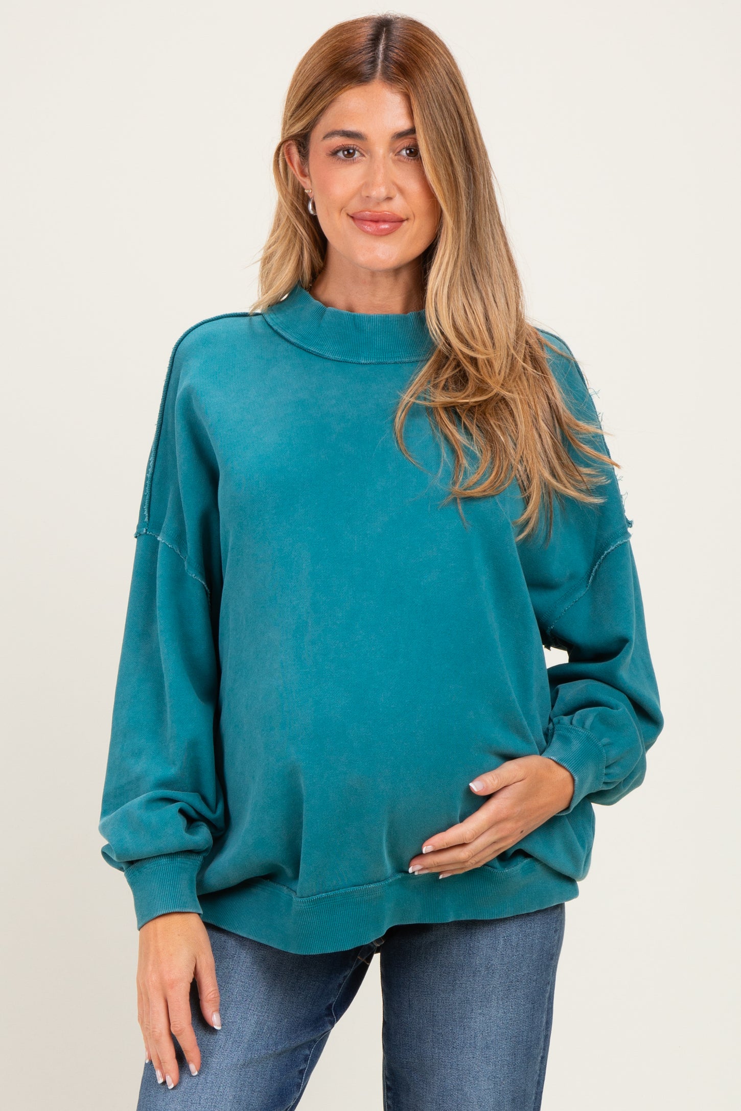 woman wearing a teal maternity sweatshirt with a relaxed fit, holding her baby bump