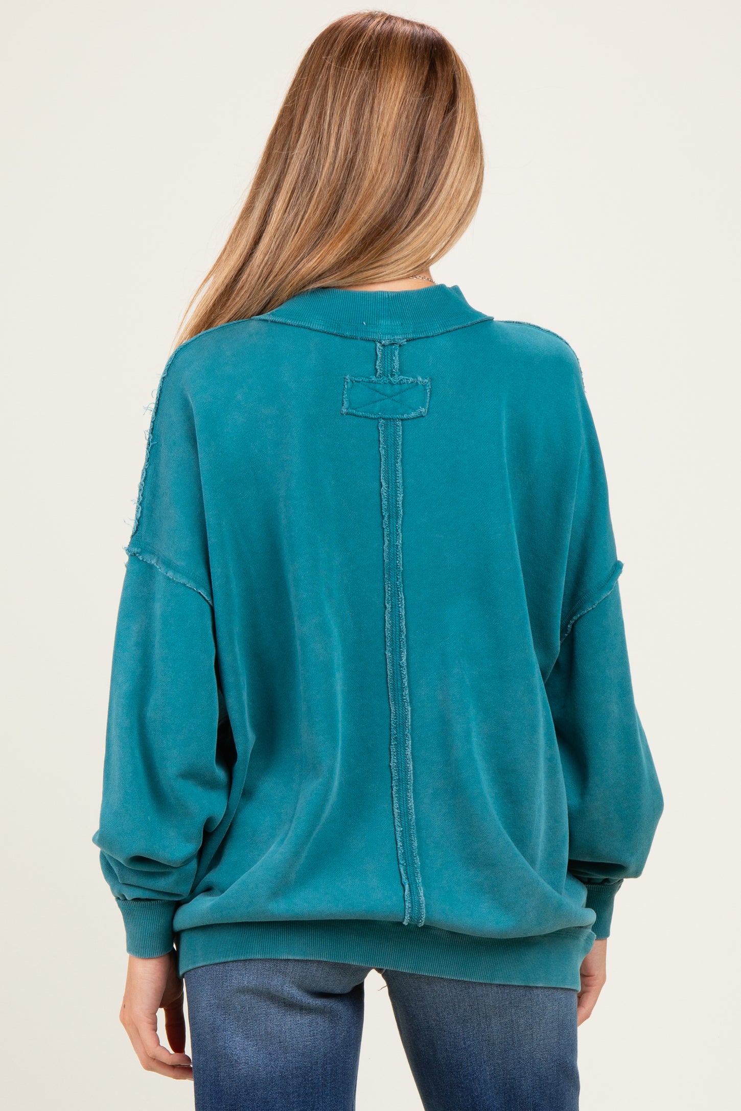 woman wearing a teal oversized maternity sweatshirt with a back seam detail, featuring a relaxed fit and long sleeves