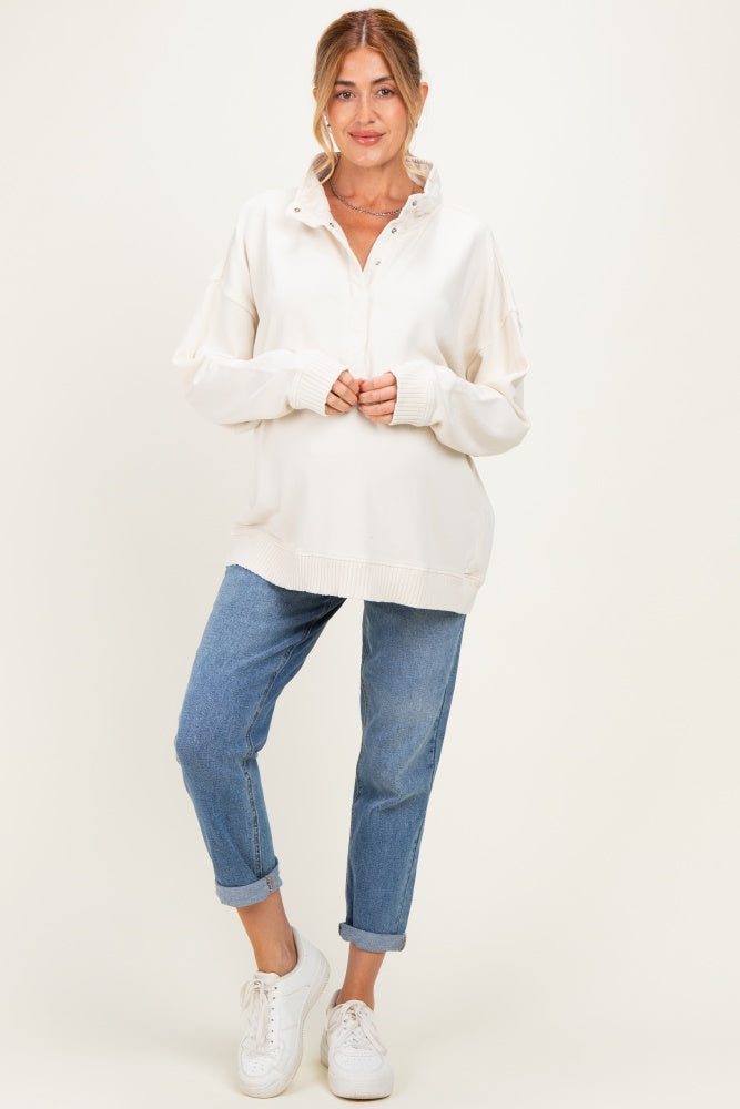 woman wearing a cream colored oversized maternity pullover with a collar and light blue rolled cuff jeans
