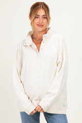 woman wearing a cream-colored maternity pullover with a buttoned collar and relaxed fit, showing her baby bump