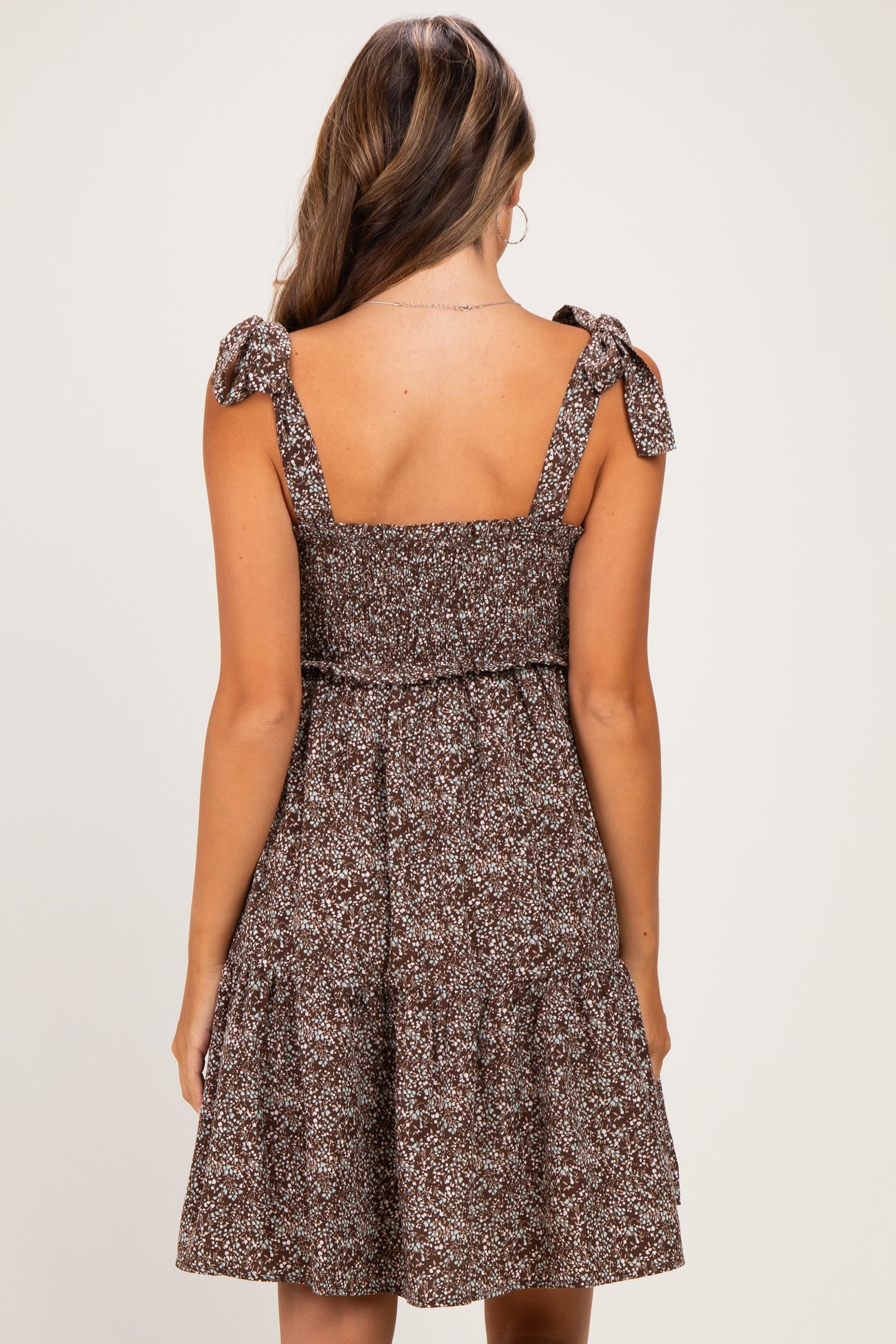 woman wearing a brown floral maternity dress with tie shoulder straps and a tiered skirt, showing her baby bump