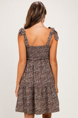 woman wearing a brown floral maternity dress with tie shoulder straps and a tiered skirt, showing her baby bump