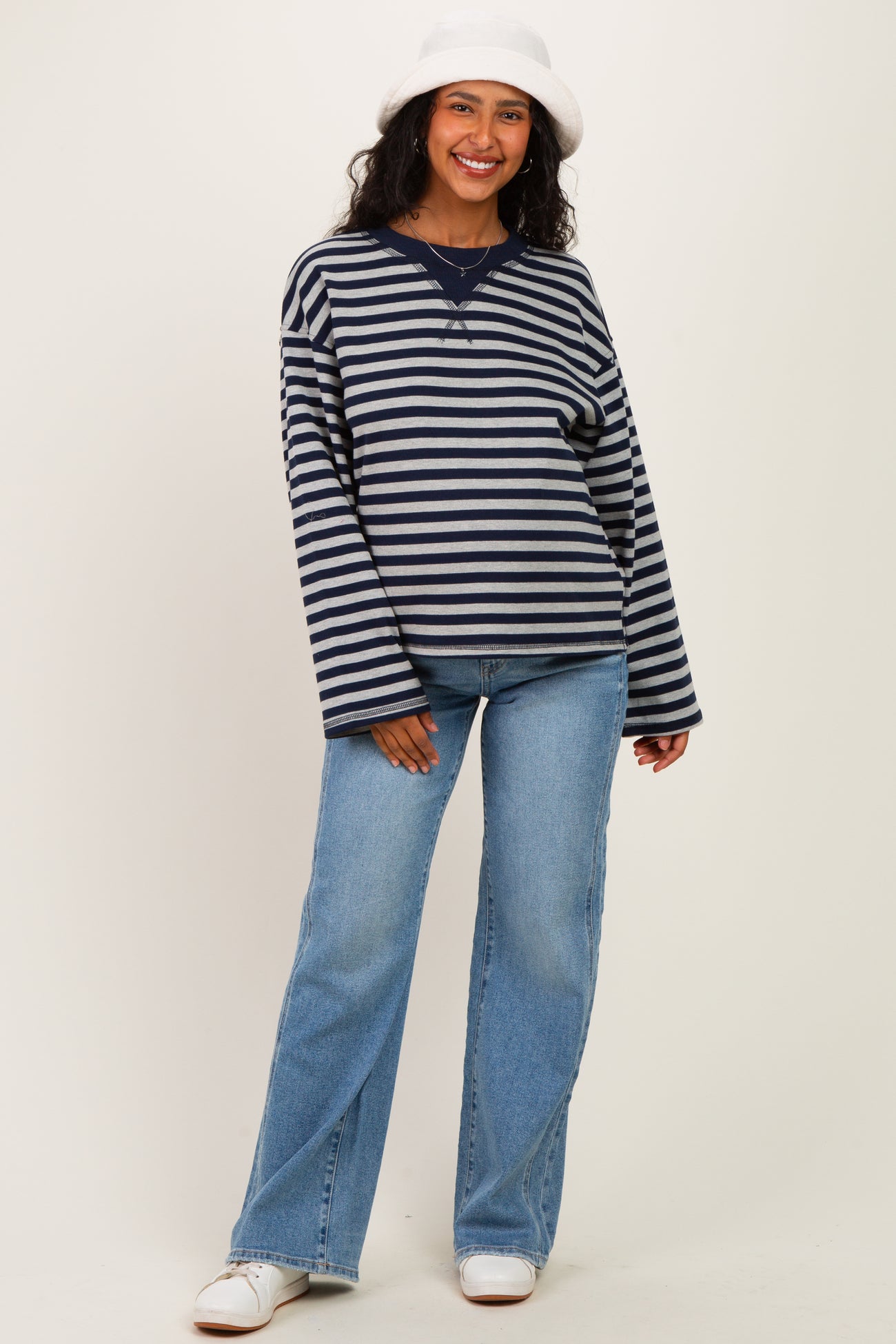woman wearing a navy and white striped maternity sweater with relaxed fit and blue jeans, smiling while standing