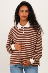 woman wearing a brown and white striped maternity top with a collared neckline and buttons, holding her baby bump