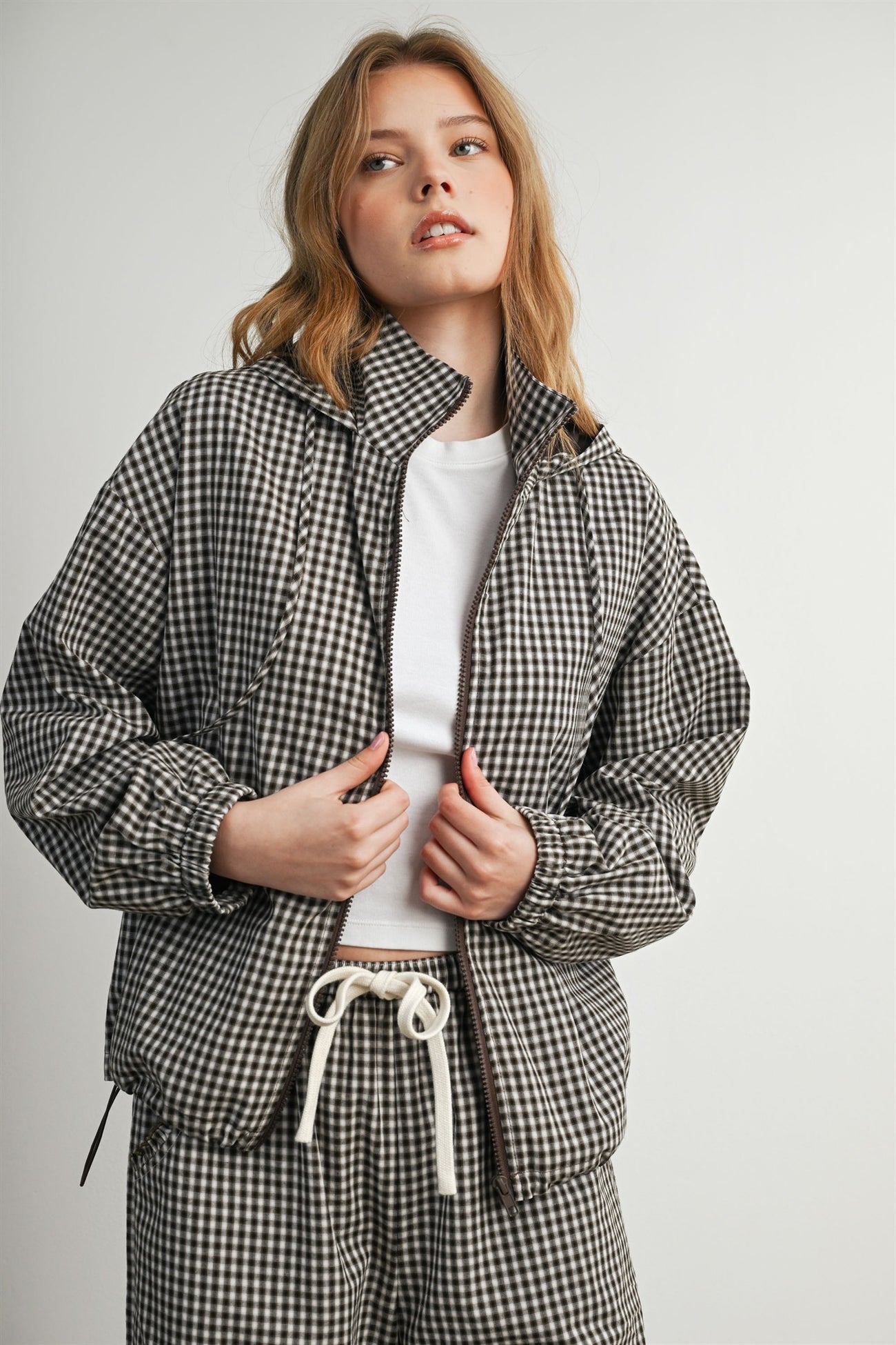 woman wearing a brown and white checkered oversized jacket with a zip front and a white t-shirt underneath