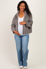 woman wearing a brown and white checkered maternity jacket, white tank top, and light blue jeans with a visible baby bump