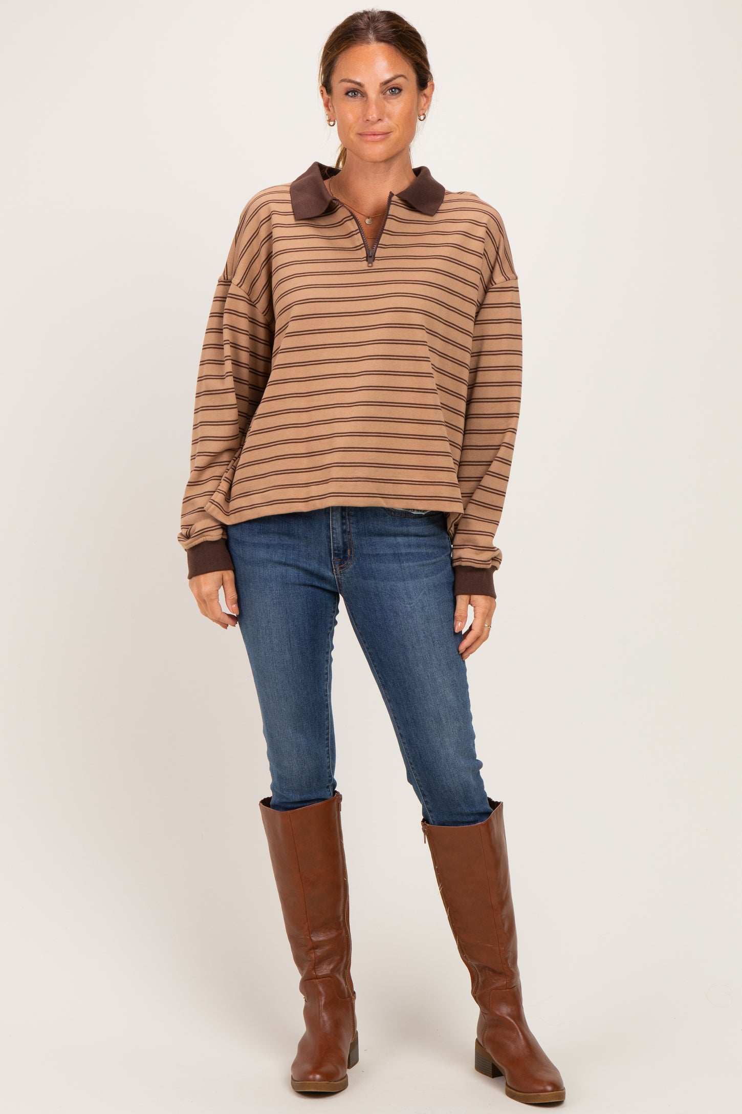 woman wearing a brown striped long sleeve polo top with a brown collar, paired with blue skinny jeans and brown knee-high boots