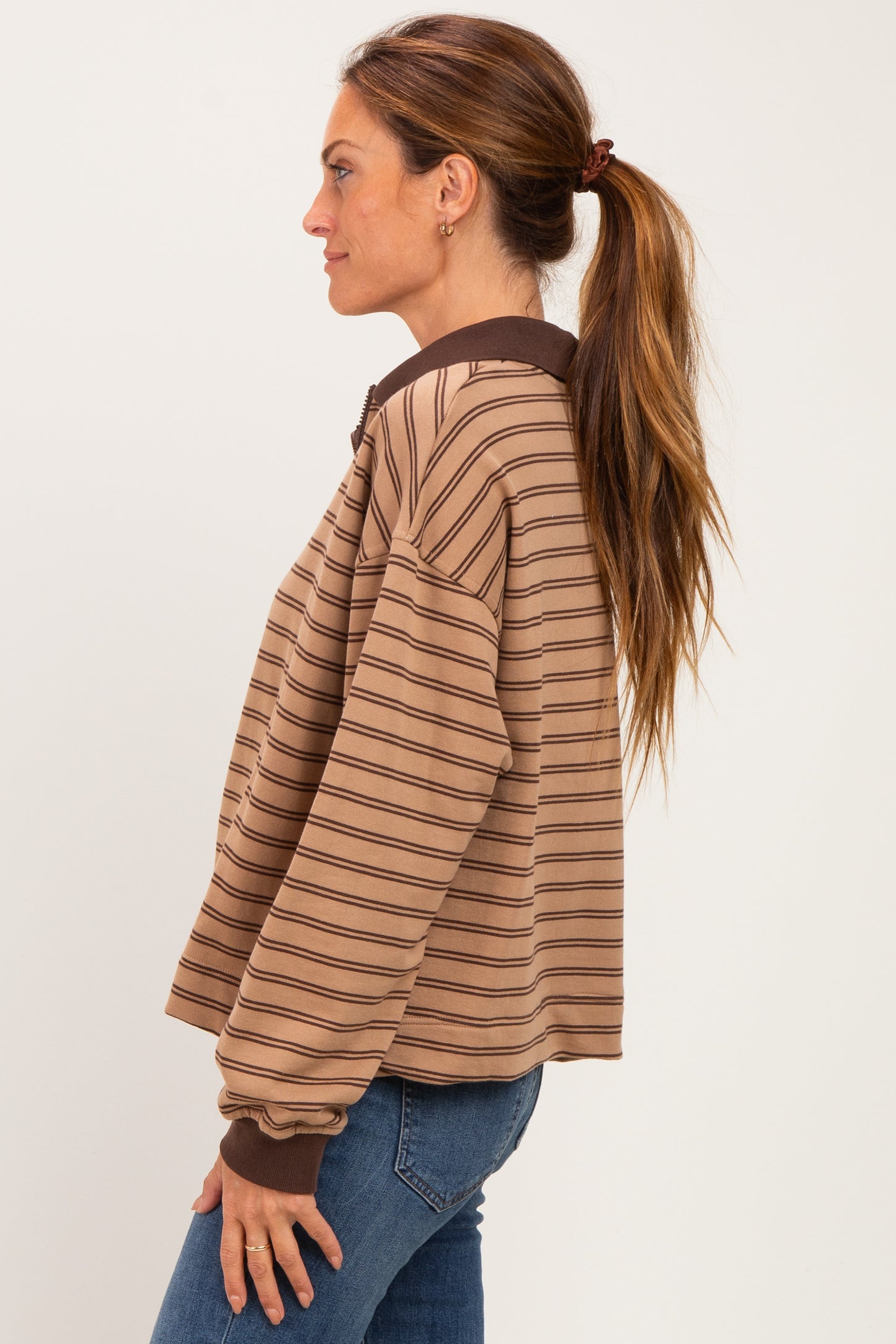 woman wearing a brown striped pullover sweatshirt with a zip collar and long sleeves, styled casually with jeans