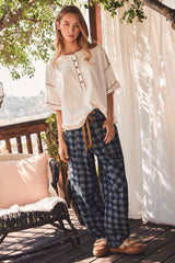 woman wearing a cream-colored button-up top with short sleeves and blue plaid wide-leg pants