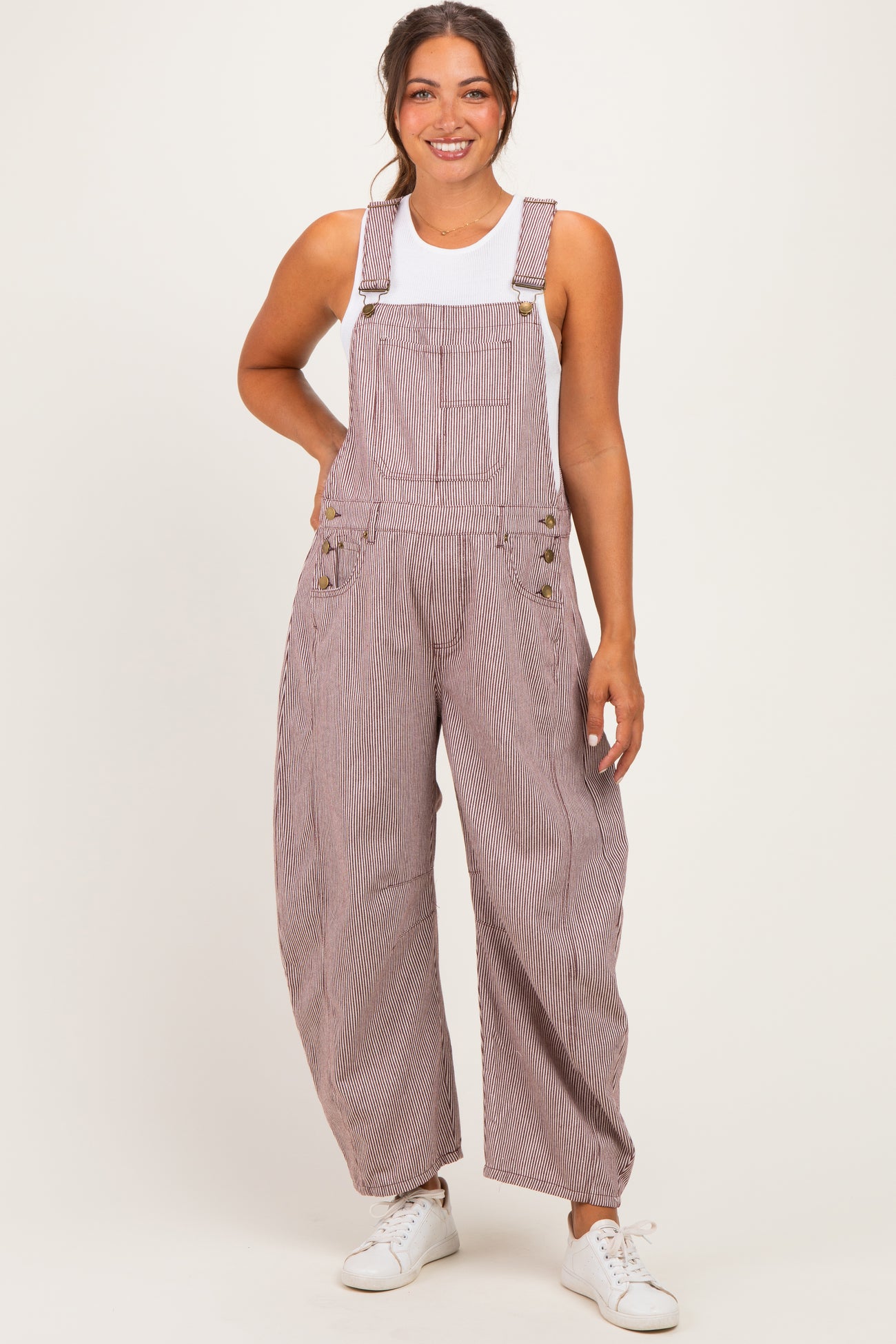 woman wearing a striped maternity overall with wide legs and a white tank top, smiling and posing