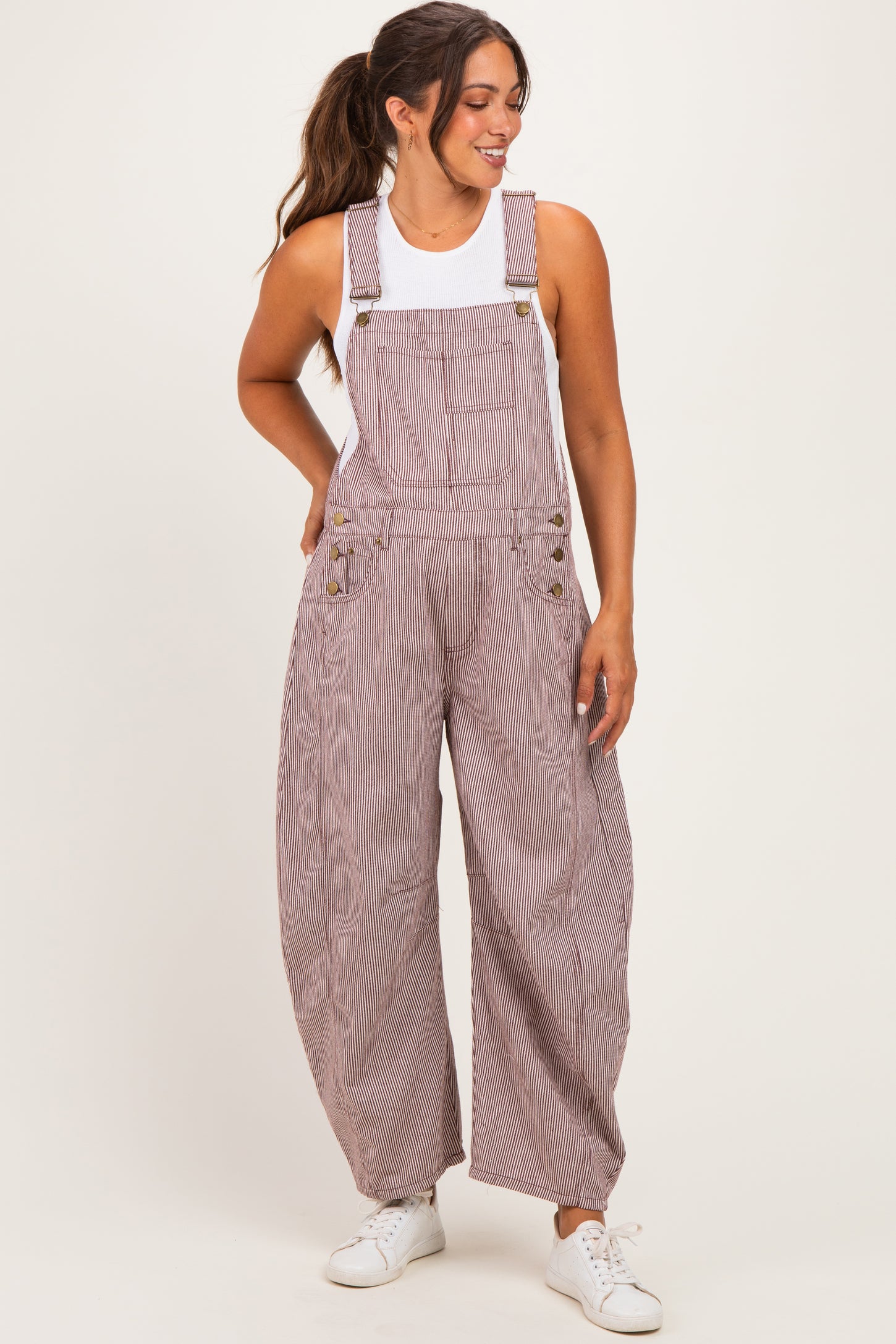 woman wearing a striped maternity overall with wide legs and a white tank top, styled with casual white sneakers