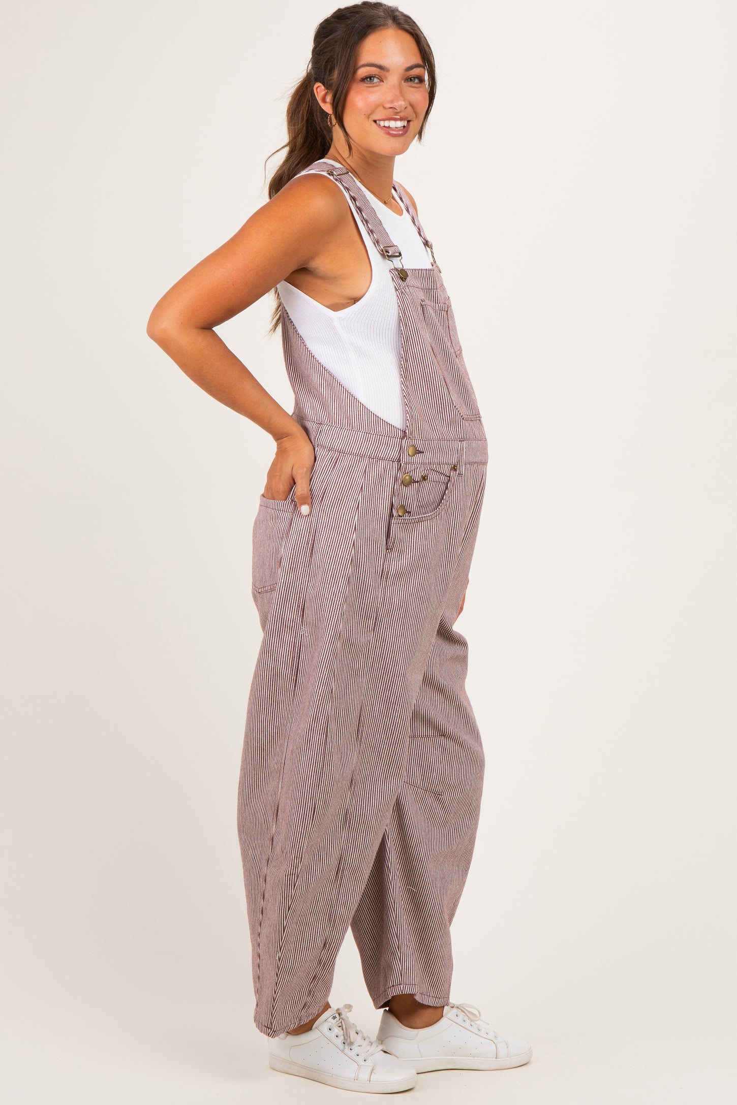 woman wearing a striped maternity overall with buttons and pockets, showing her baby bump in a side profile view