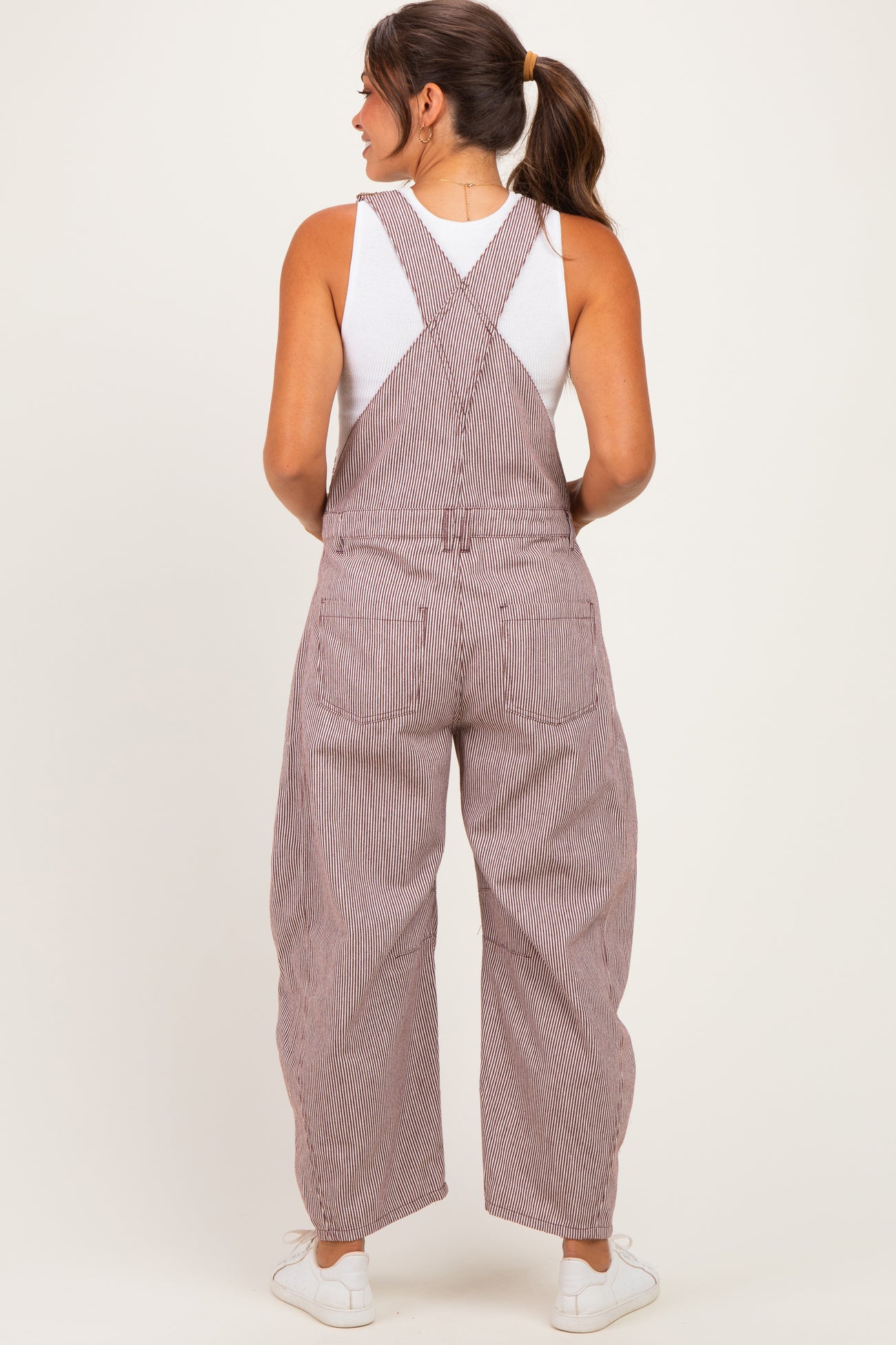 woman wearing striped maternity overalls with a loose fit and a white tank top underneath, showing a relaxed back view