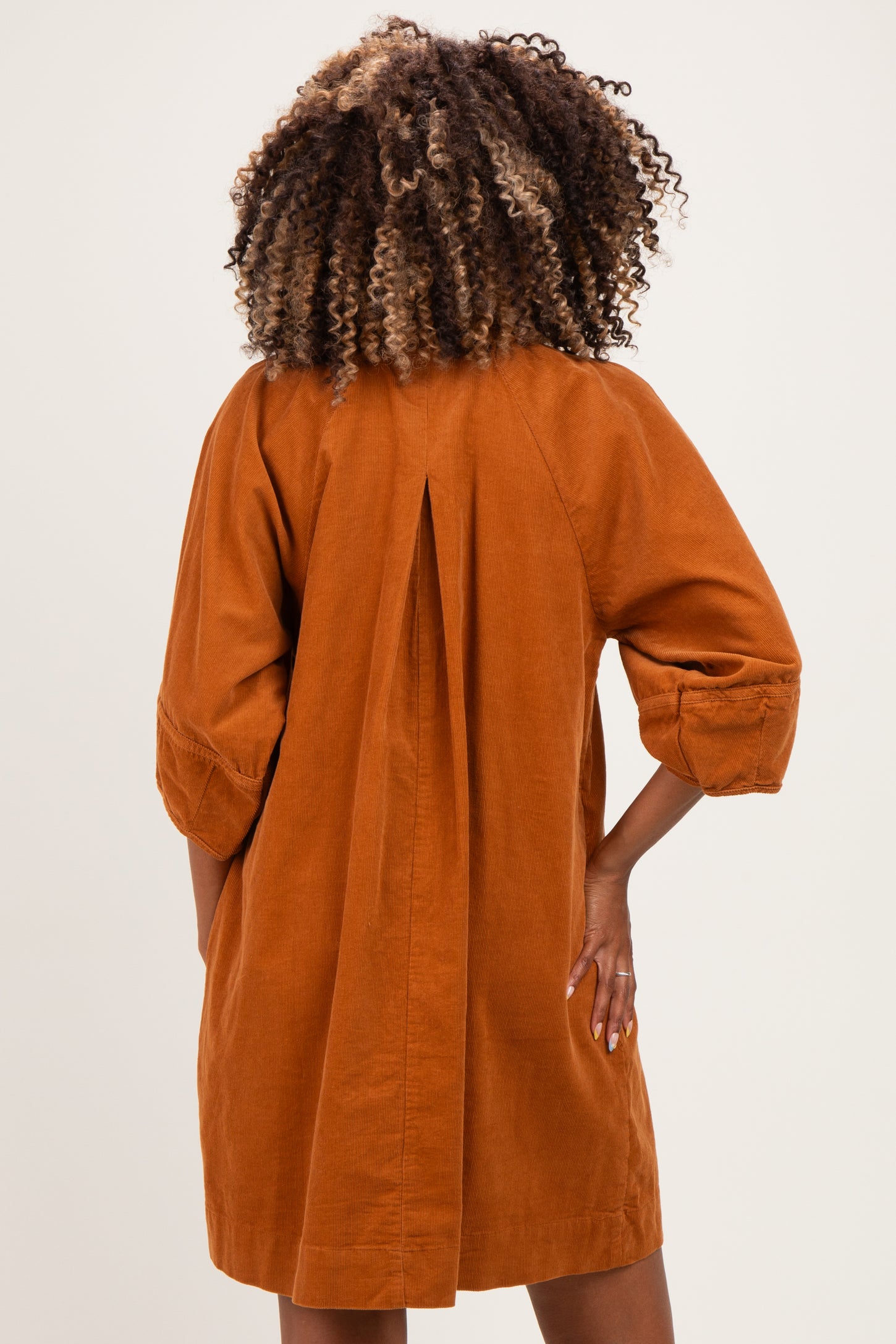 woman wearing an orange corduroy maternity dress with a back pleat and three-quarter sleeves