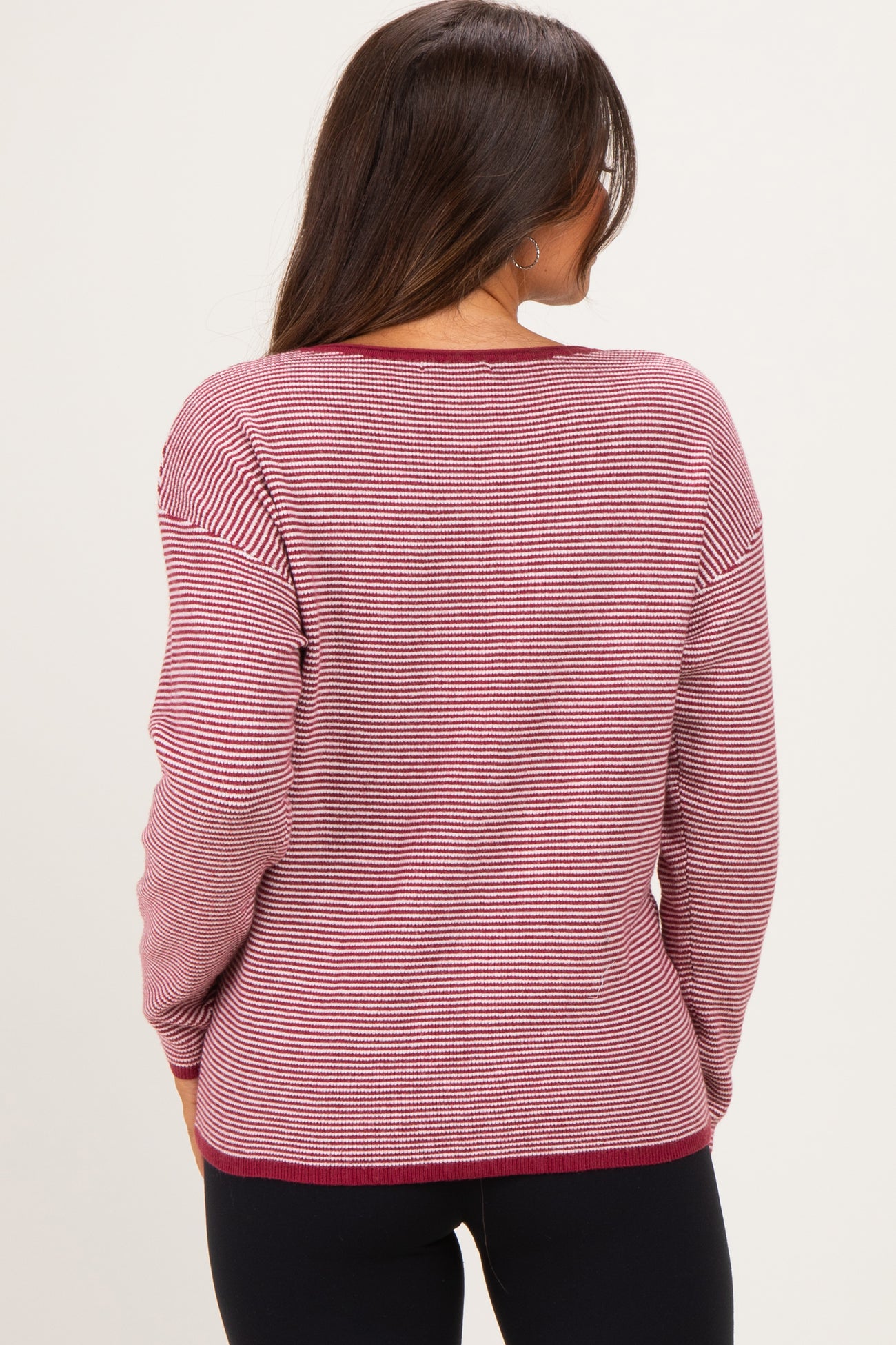woman wearing a maroon and white striped maternity sweater, view from the back, paired with black leggings