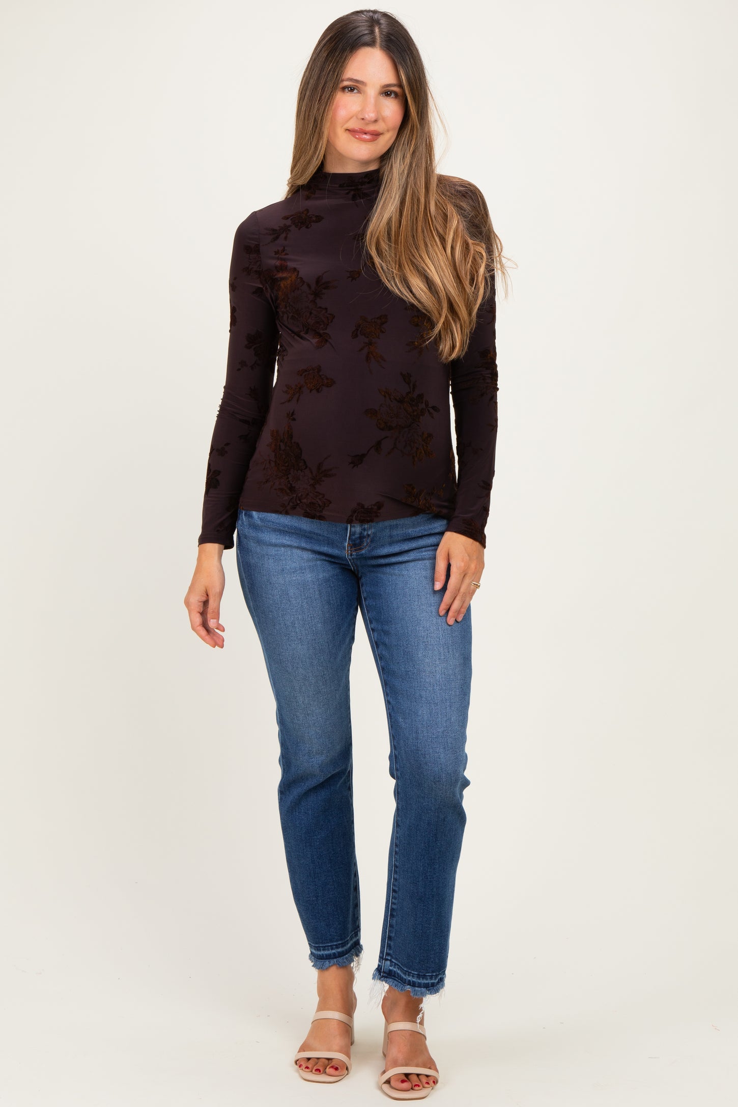woman wearing a dark brown long sleeve maternity top with floral patterns and blue jeans