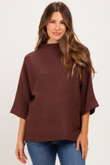 woman wearing a brown maternity top with a high neckline and short sleeves, paired with blue jeans
