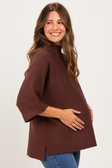 woman wearing a brown maternity top with short sleeves and a relaxed fit, cradling her baby bump