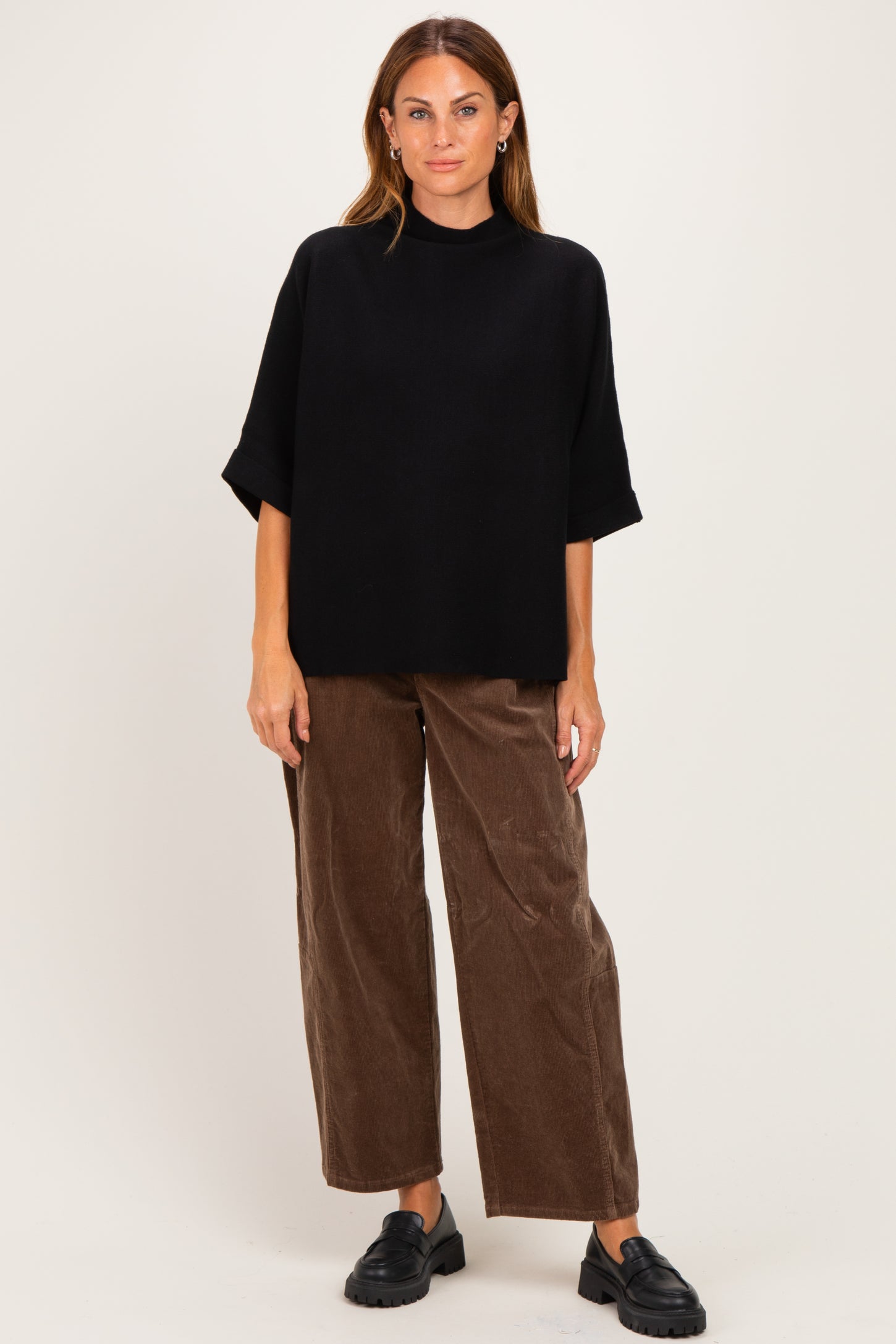 woman wearing a black oversized knit top and brown wide-leg corduroy pants, paired with black slip-on shoes