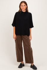 woman wearing a black oversized knit top and brown wide-leg corduroy pants, paired with black slip-on shoes