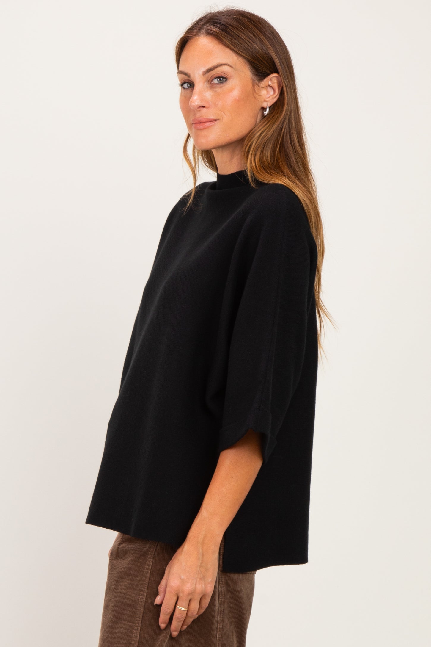woman wearing a black oversized sweater with a high collar and wide sleeves, styled casually with brown pants