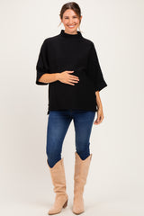 woman wearing a black short sleeve maternity top and holding her baby bump with blue jeans and beige boots