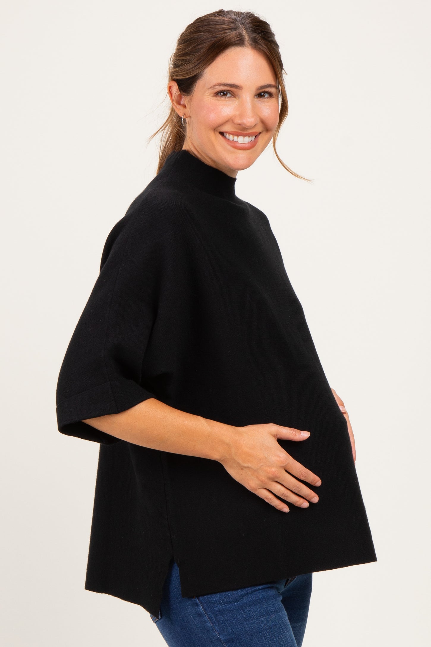 woman wearing a black maternity poncho top with a high neckline and a visible baby bump