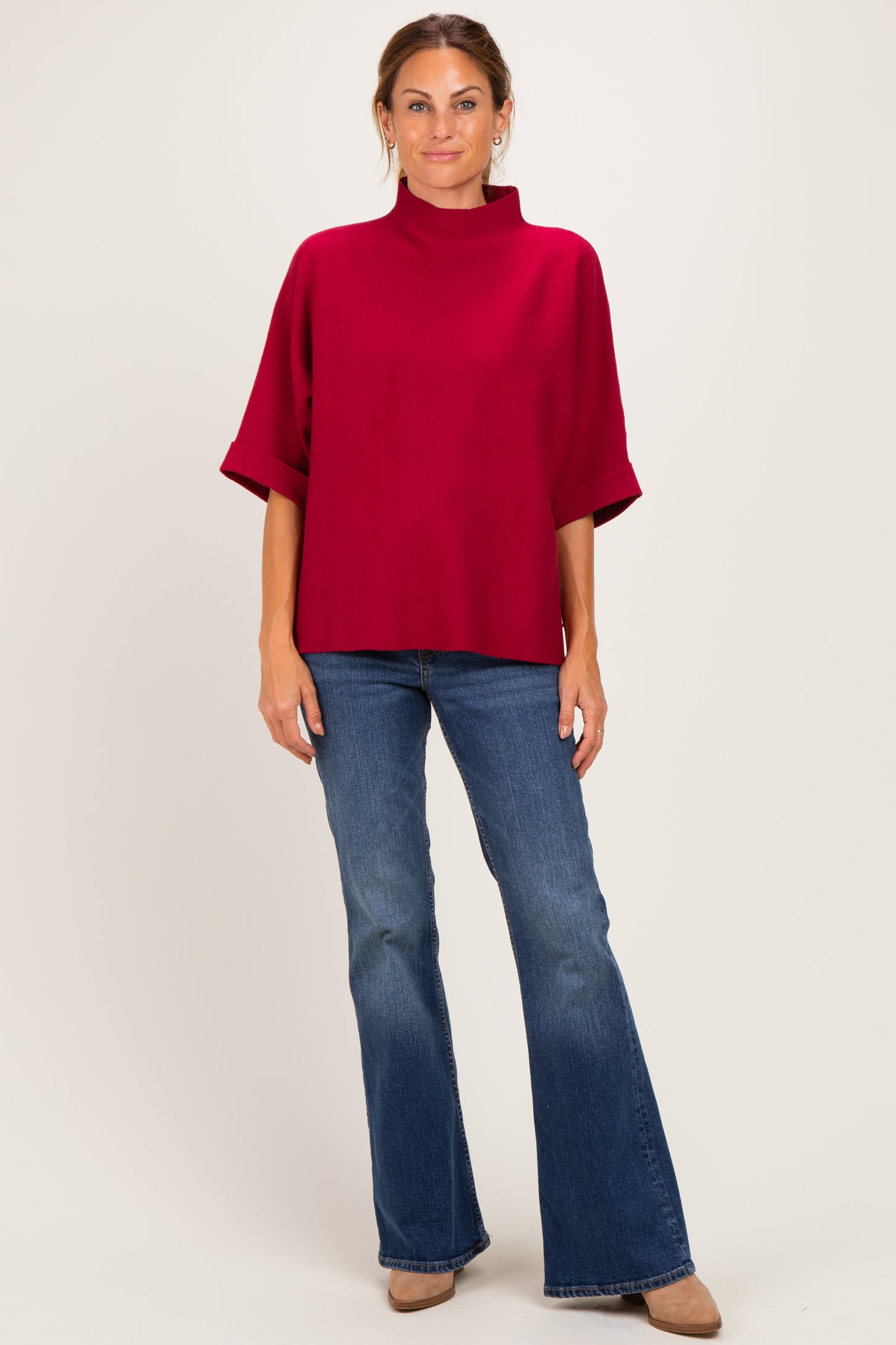 woman wearing a burgundy mock neck top with wide sleeves and blue flared jeans