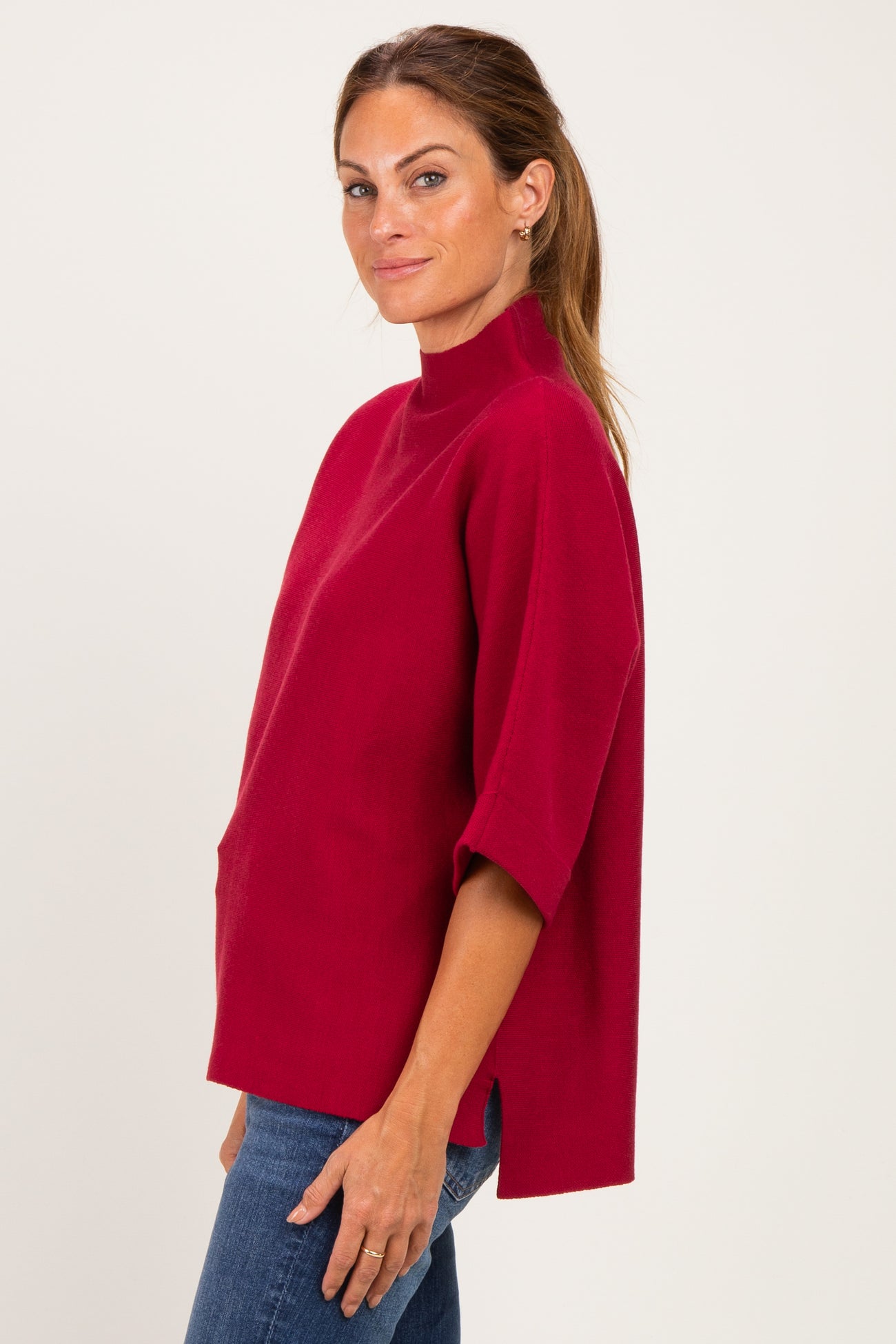woman wearing a red short sleeve mock neck top with side slits and a relaxed fit, paired with blue jeans